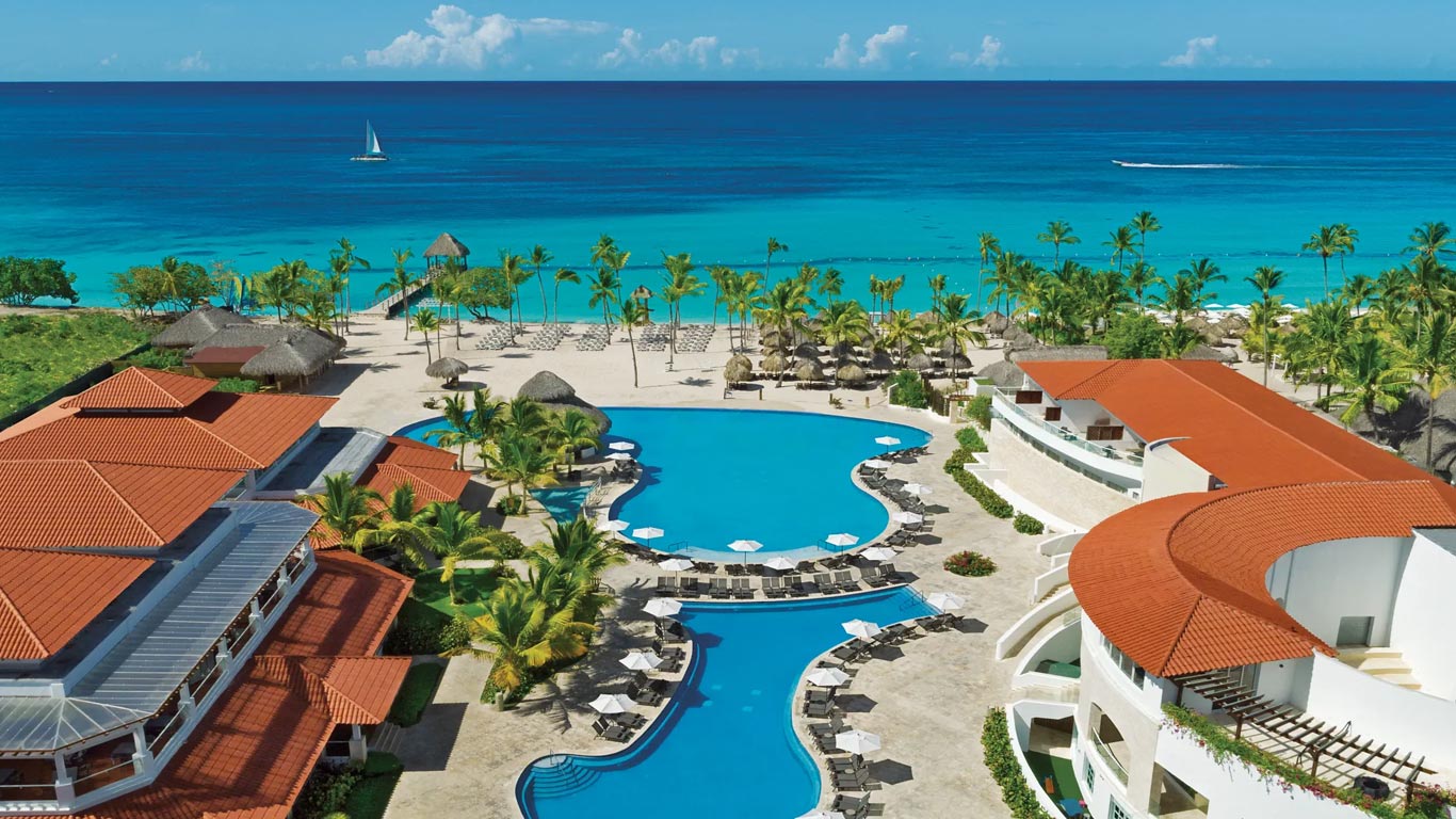 Piscina del hotel rodeada de palmeras, con el mar al fondo