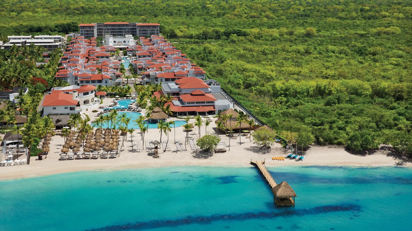 Vista aérea del hotel, de techos rojos, entre la selva y la playa, con un muelle de techo de paja